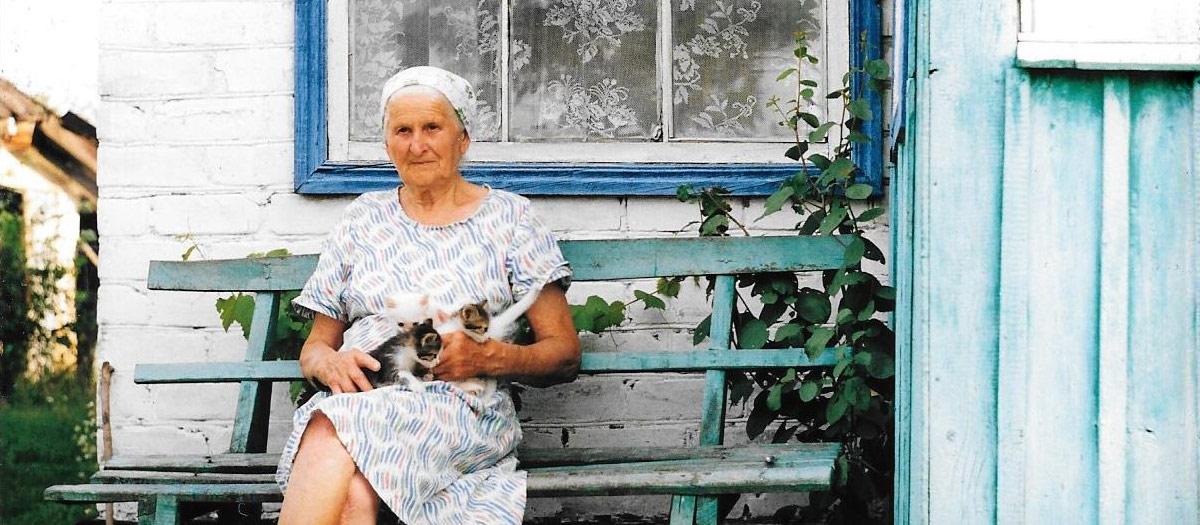 乌克兰，一位老妇人坐在自家门外的长椅上，腿上坐着三只小猫.